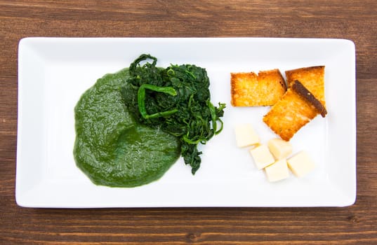 Tray with creamed spinach and croutons on wooden table seen from above