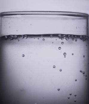 Glass of sparkling water soft drink closeup on carbon dioxide gas bubbles.