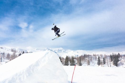 Free style skier performing a high jump. Ski lifts in the mountains in the background. 