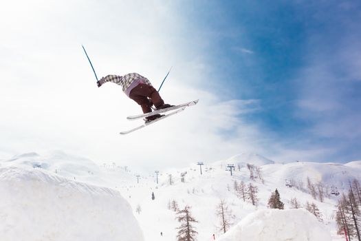 Free style skier performing a high jump. Ski lifts in the mountains in the background. 