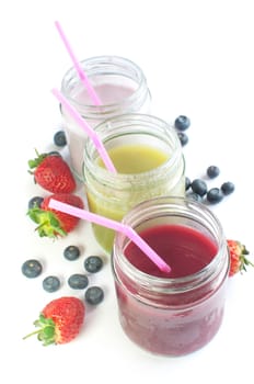 Chilled fruit smoothies in jars over a white background with fruit