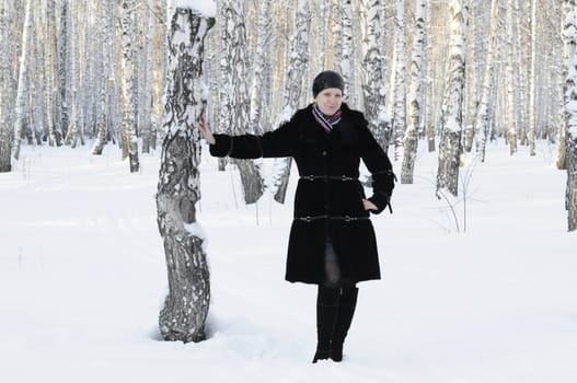 The woman in a black fur coat costs in the birch wood in the winter