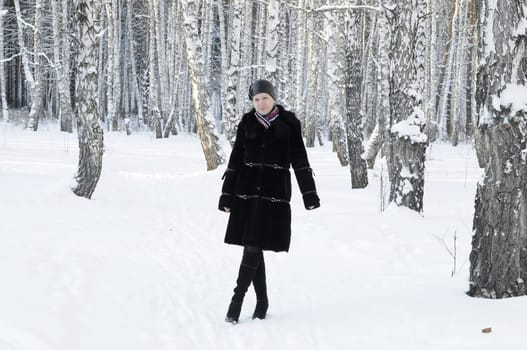 The woman in a black fur coat costs in the birch wood in the winter