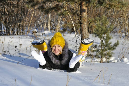 The joyful young woman lies on snow near a pine in park