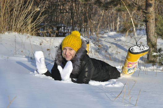 The joyful young woman lies on snow near a pine in park