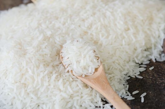 white rice  grains with wooden spoon on wooden table