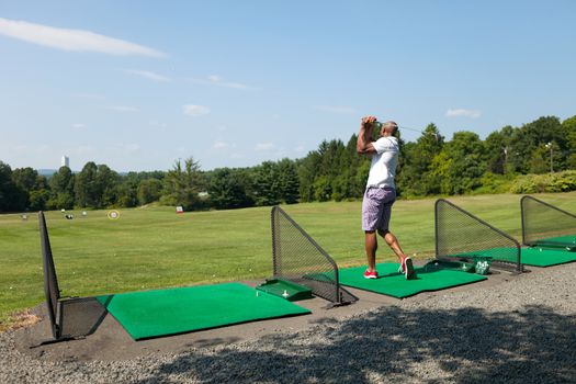 Athletic golfer swinging at the driving range dressed in casual attire.