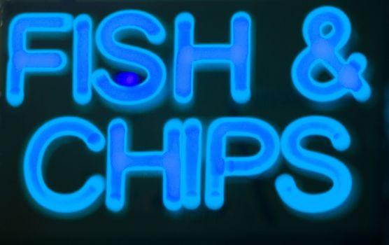 Fish and chips restaurant neon sign at night in street photo.