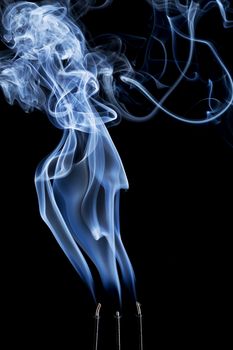 delicate smoke plume and swirls from  burning three incense sticks