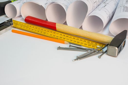 Drawing rolls, hammer, nails, builder's level, pencil, tri-square on white surface