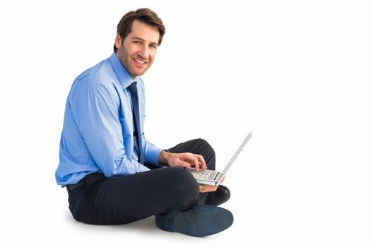 Smiling businessman sitting on floor working on laptop on white background
