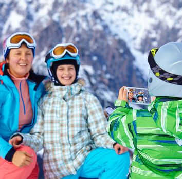 Ski, winter, snow, skiers, sun and fun - boy photographed family on phone during winter vacations.