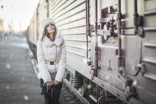 Young woman in fur hat and down jacket on a railroad station