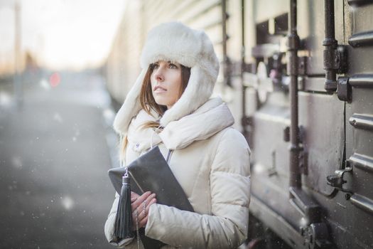 Young woman in fur hat and down jacket near the cargo carriage