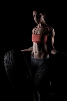 fitness girl lifting tyres, against black background