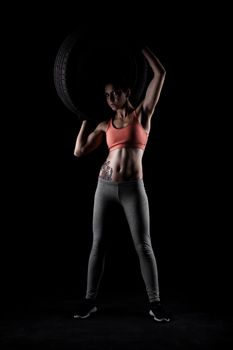 fitness girl lifting a tyre, against black background