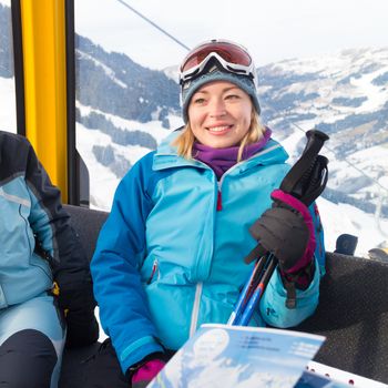 Cheerful lady in gondola enjoing the snowy mountain view, excited before skiing.