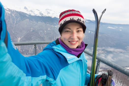 Cheerful lady taking selfie enjoing the snowy mountain view, excited before skiing.