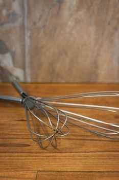 Well used metal wisks lay on a wooden counter.