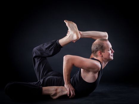 Handsome man doing yoga. Shot on black background