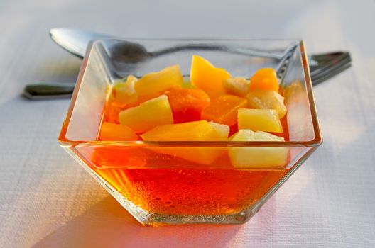 On the tablecloth table in a glass vase are pieces of fruit in sugar syrup.