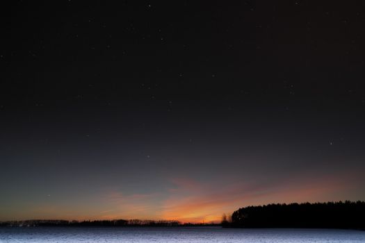 Sunset in the field. Evening smoothly into the night. Agricultural field covered by snow.