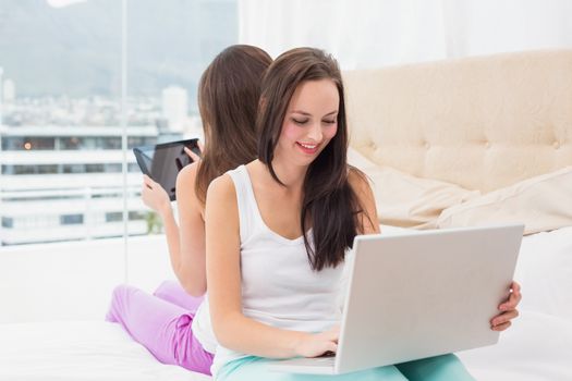 Pretty friends using their technology on bed at home in the bedroom