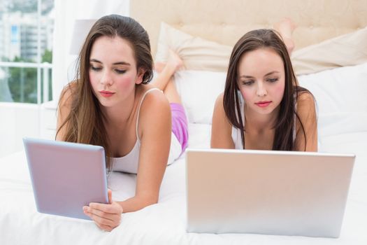 Pretty friends using their technology on bed at home in the bedroom