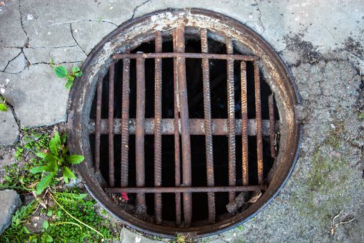 Manhole with the handmade metal armature cover in the cracked concrete and asphalt surface