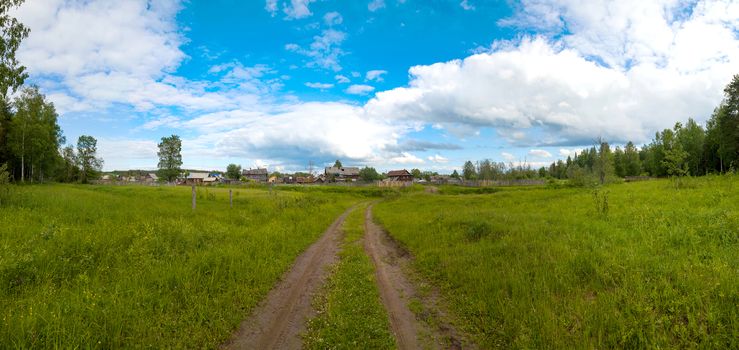 Country road in a green field leading to the village