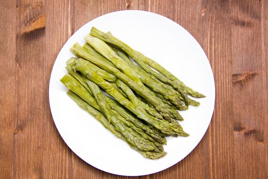 Cooked asparagus on plate on wooden table seen from above