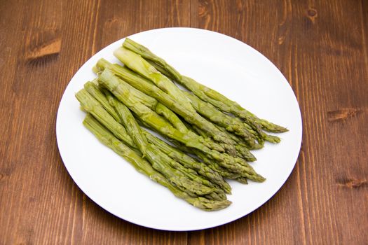 Cooked asparagus on plate on wooden table