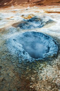 Mudpot in the geothermal area Hverir, Iceland. The area around the boiling mud is multicolored and cracked. 