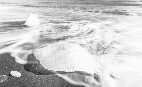 Beautiful beach in the South of Iceland with a black lava sand is full of icebergs washed by the sea. Black and white with a long exposure