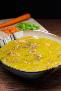 A bowl of fresh split pea soup with carrots, onions, and ham plus ingredients in the backgound.