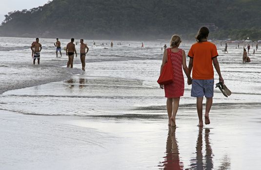 SAO SEBASTIAO, BRAZIL - JANUARY 04, 2015: An unidentified couple walking along a crowed beach at sunset in Brazil in the summer.