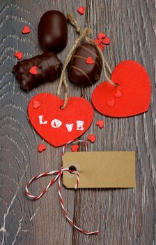 Two Red Hearts with Word Love, Blank Gift Card and Chocolate Candies closeup on Dark Wooden background