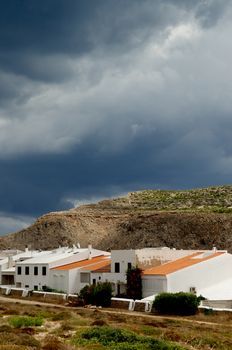 Classic Houses in Small Menorca Urbanization between Hills under Cloudy Skies Outdoors. Balearic Islands