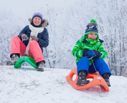 Winter, play, fun - Cute little boy and his mother having fun with sled in winter park