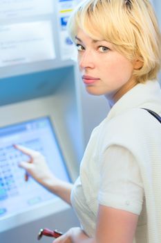 Lady buying a railway ticket at the automatic ticket vending machine with touch screen.