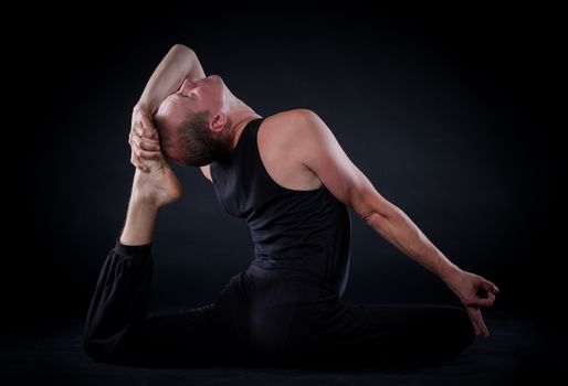 Handsome man doing yoga. Shot on black background