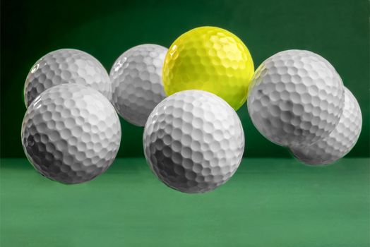 Six white and one yellow golf balls suspended in mid air on a green bacground.