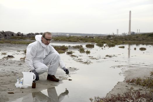 
Worker in a protective suit examining pollution in the water at the industry.