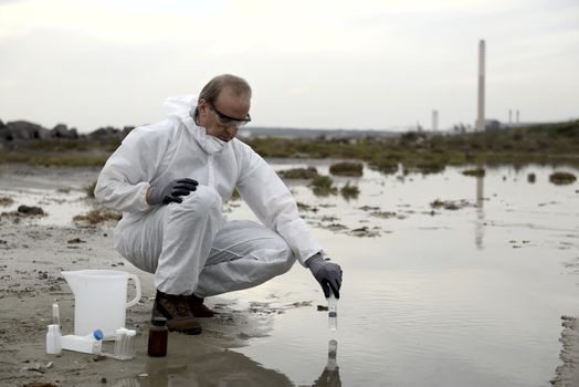 
Worker in a protective suit examining pollution in the water at the industry.