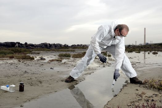 
Worker in a protective suit examining pollution in the water at the industry.