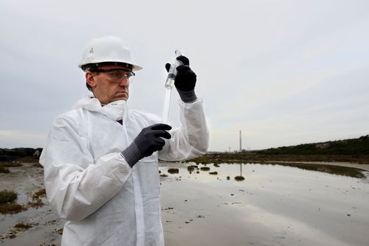 
Worker in a protective suit examining pollution in the water at the industry.