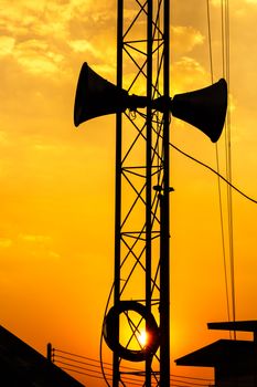 loudspeaker on metal pillar above roof of house in twilight time at Thailand (silhouette style)