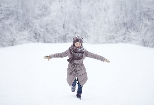 Little girl running on the background of snow covered winter park