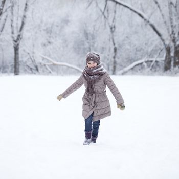 Little girl running on the background of snow covered winter park