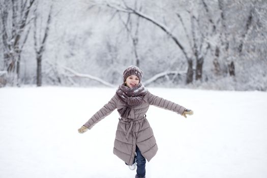 Little girl running on the background of snow covered winter park